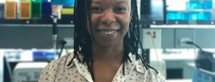 Headshot of Thelma Madzima. In the background are a series of pipette tip boxes and a mini vortexer.