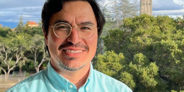 Headshot of Jose Dinenny iwith the skyline of Palo Alto behind him.